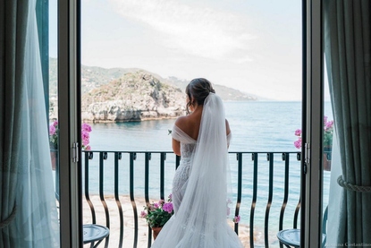 Bride dressed and ready on her balcony looking out to sea in Mazzaro Bay Taormina Mare